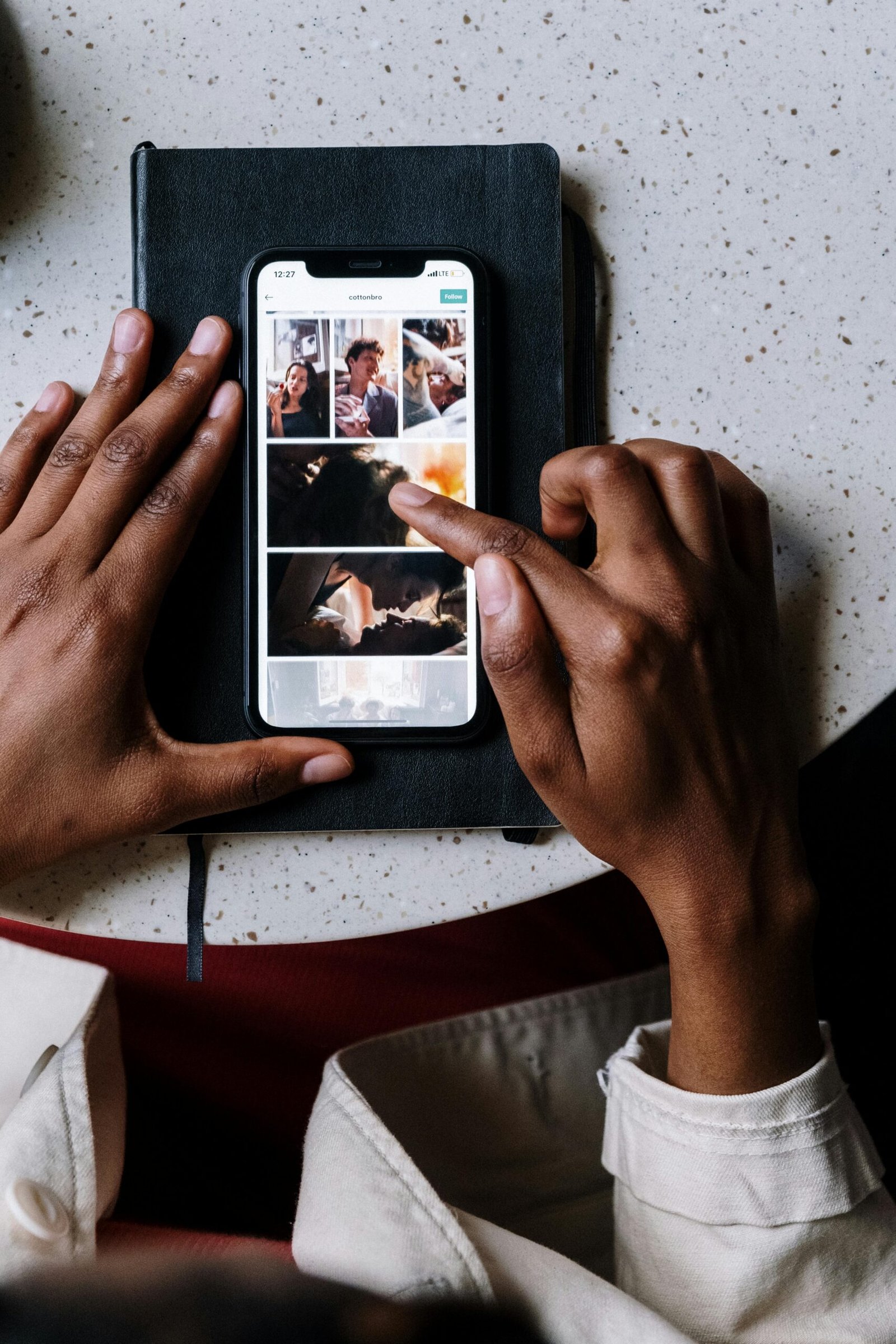 Overhead view of hands using smartphone on top of a notebook, browsing through images on screen.